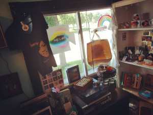 michelle obama shirt, vintage stereo, shelves with mugs, books, neon rainbow in window looking out on street