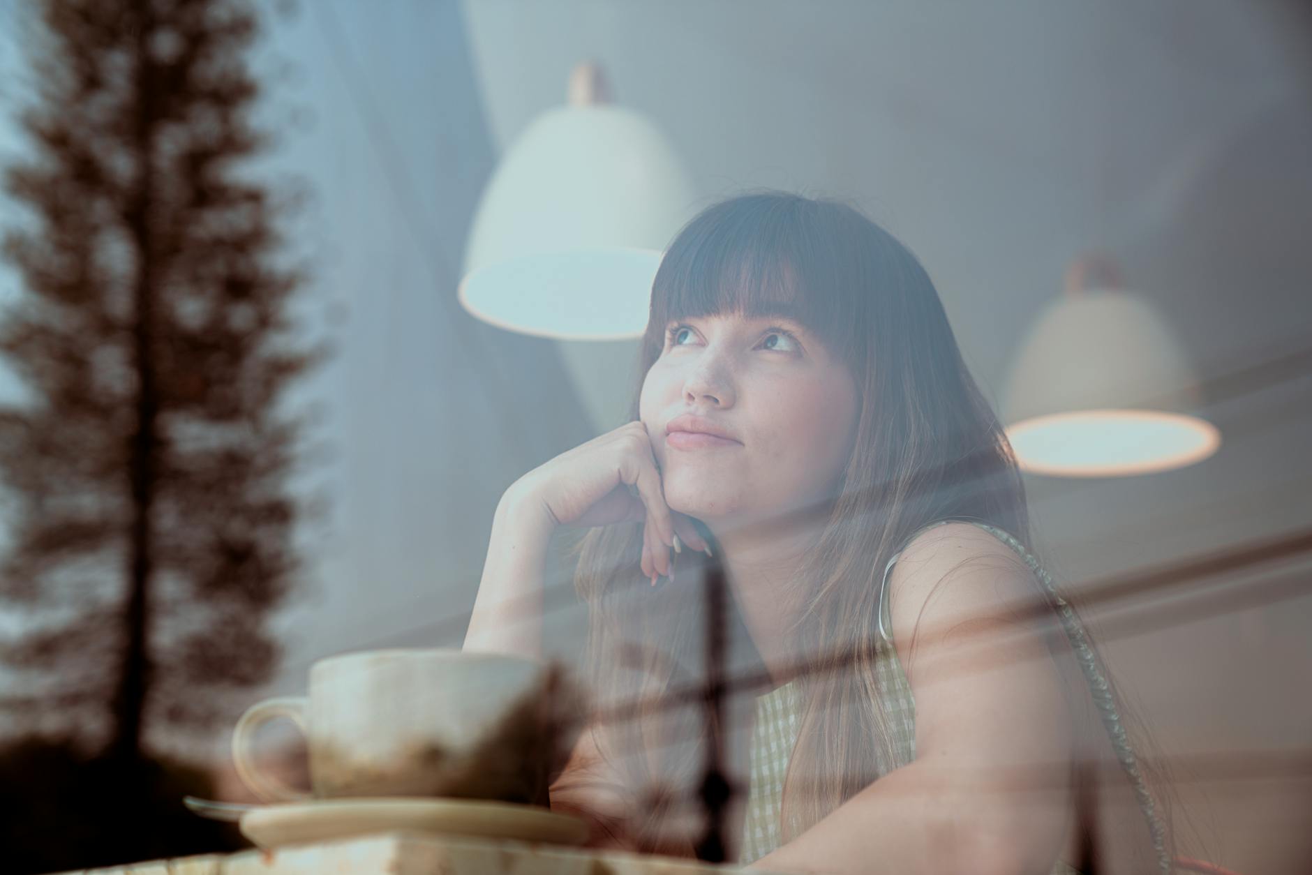 woman looking out a window drinking a cup of something
